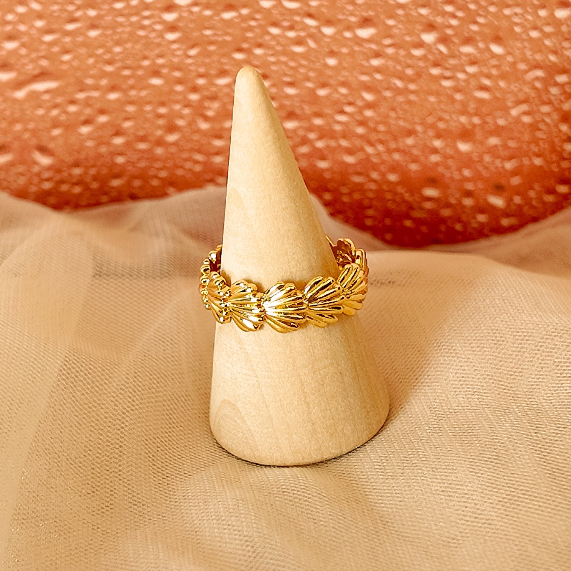 Gold ring on a white cone against a textured pinkish-beige background