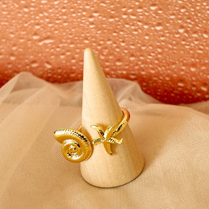 Gold ring with decorative elements on a beige cone-shaped stand against a textured pink background.