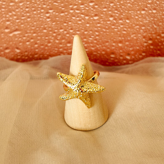 Gold starfish ring on a wooden cone with a textured beige background